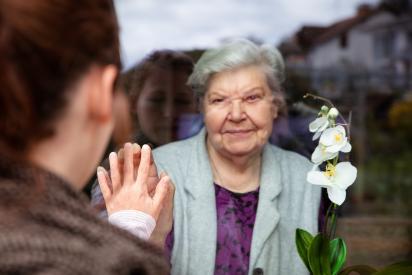 Foto von einer alten Frau hinter einer Glasscheibe, die Besuch empfängt
