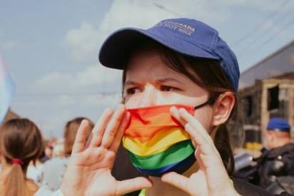 Demoszene: Person mit Regenbogenmaslke uns Basecap hält rufend die Hände vor dem Mund