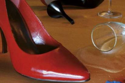 Roter Stöckelschuh, umgekipptes Sektglas, Kondomverpackung auf Holzfußboden